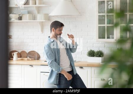 Fröhlicher gutaussehender Mann, der allein in der Küche zu Musik tanzt. Stockfoto