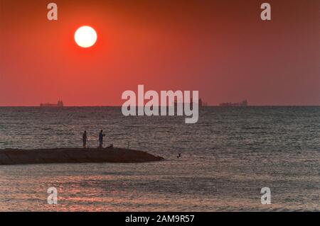 Männer, die am Seawall Boulevard Pier angeln, Schiffe auf dem Weg zum Hafen, bei Sonnenaufgang in Galveston, Texas, USA Stockfoto