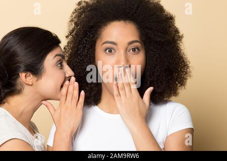 Überraschte das afroamerikanische Mädchen, das dem geheimnis eines indianischen Freundes zuhörte. Stockfoto