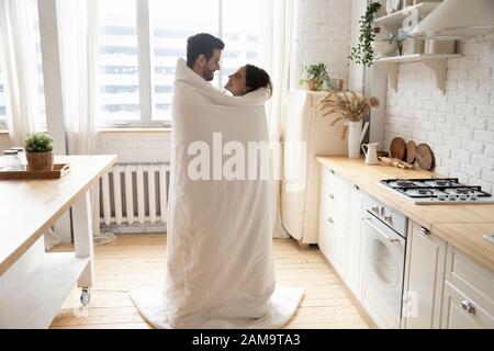 Fröhliches junges Familienpaar in der Küche, bedeckt mit Decke. Stockfoto