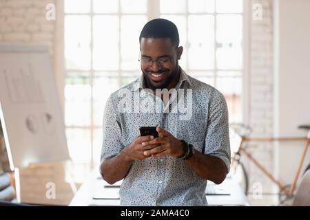 Lächelnder, biracialer männlicher Mitarbeiter, der das Handy im Sitzungssaal des Büros verwendet Stockfoto