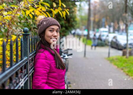 Asiatisches Mädchen mit Frechheit und ungewöhnlichem Aussehen. Attraktives Mädchen in pinkfarbener Jacke und Strickmütze. Verschwommener Hintergrund mit Bokeh. Stockfoto