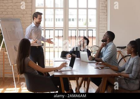 Lächelnde männliche Moderatorin spricht bei der Unterweisung mit aufgeregten multiethnischen Arbeitern Stockfoto