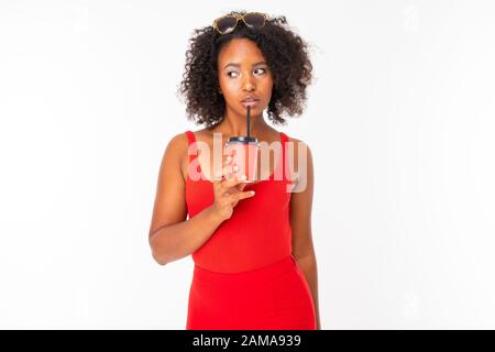 Afrikanisches Mädchen in roter Kleidung trinkt Kaffee aus einer Tasse mit Strohhalm auf weißem Hintergrund. Stockfoto