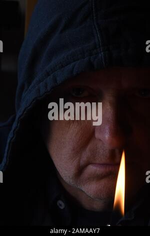 Schattenhafte Nahaufnahme älterer Menschen Gesicht mit leichterer Flamme im Vordergrund Stockfoto