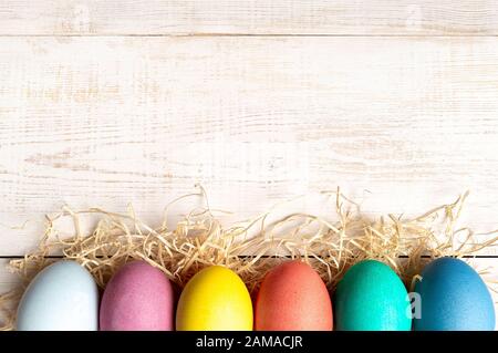 Osterkonzept. Bunte Eier auf weißem Holzhintergrund mit Platz für Text. Draufsicht oder flache Lage Stockfoto