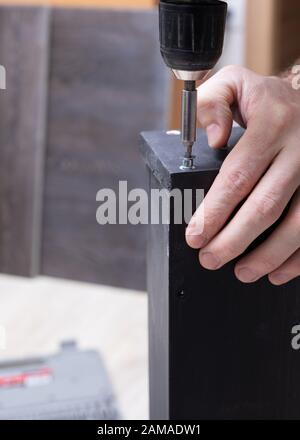 Nahaufnahme Mann Arbeiter in Arbeitskleidung Arbeiten mit Schraubenzieher in den Händen ist die Montage von Möbeln. Stockfoto