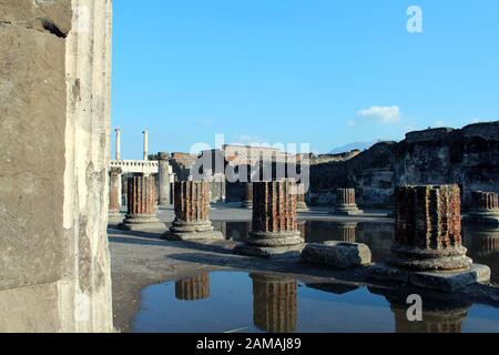 Eine Reihe von Säulen bleibt von Pompeji unter klarem blauen Himmel mit Reflexionen auf Wasser. Stockfoto