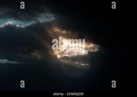 Vollmond in einer übergiebelten Nacht mit Lichtstrahlen, die aus einem Loch in den Wolken kommen Stockfoto