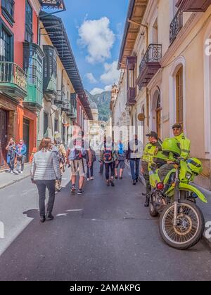 Bogota, Kolumbien - 12. September 2019: Straße von Bogota mit bunten Häusern aus der Kolonialzeit, Menschenmenge, Polizeimann mit Motorrad und Berg VI Stockfoto