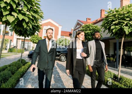 Team von multiethnischen Geschäftsleute zwei Männer und Frauen in eleganter Freizeitkleidung, die auf dem Geschäftstreffen draußen spazieren gehen. Frau hält digitales Tablet Stockfoto