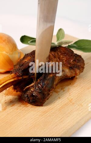 Lammbeinbraten langsam gekocht auf Holzschneidebrett mit Zwiebel und frischen Minzblättern. Frühling, Osterabendessen. Stockfoto