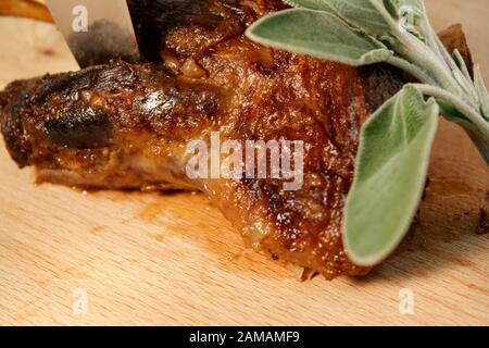 Lammbeinbraten langsam gekocht auf Holzschneidebrett mit Minzblättern. Frühling, Osterabendessen. Stockfoto