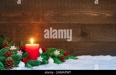 Weihnachten oder Advent Holzhintergrund mit brennender roter Kerze auf Schnee, dekoriert mit Tannenzweigen und Verzierungen. Kopierbereich Stockfoto