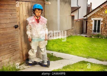 Trauriges kleines Kind mit Hoverboard und überschützter Mutter, die einen Jungen in einer Blase umhüllte, um supersicher zu sein Stockfoto