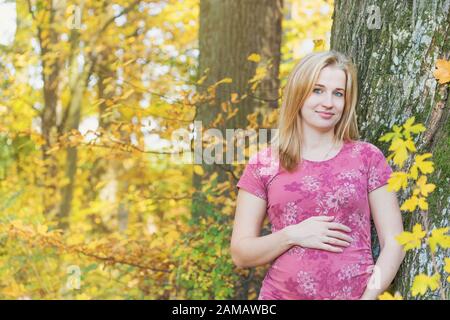 Porträt der schwangeren jungen Frau, die im Freien mit Blick auf die Kamera posiert. Horizontal. Stockfoto