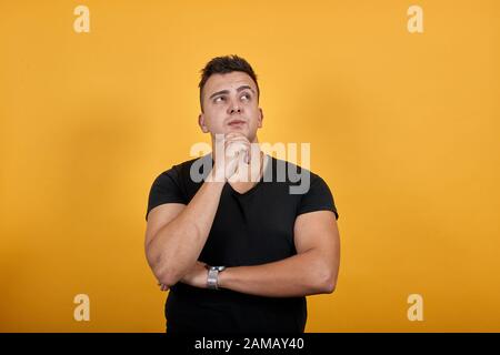 Konzentrierter Mann, der die Hand am Kinn hält, denkt und andere Hand am Ellenbogen hält. Stockfoto