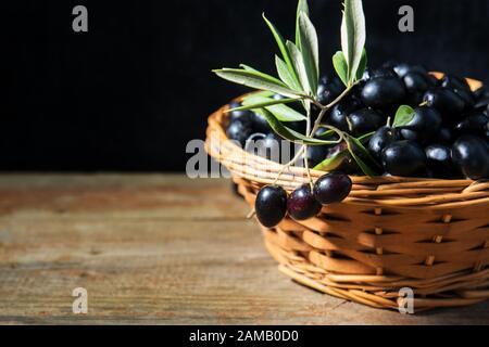 Ein wiker Korb voll mit reifen frischen schwarzen Oliven aus Apulien, Italien, Low Key Stockfoto