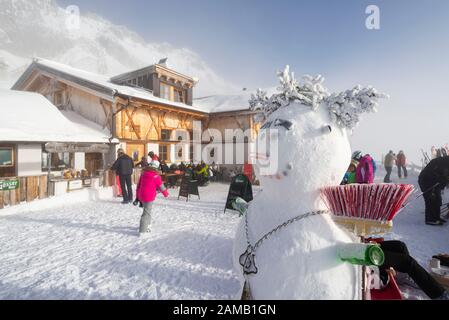 Schneemann auf der sonnigen Terrasse des schneebedeckten Hochfeldernalm-Hüttenrestaurants Grußspieße im Skigebiet Ehrwalder Alm, Österreich, Tyrol Stockfoto