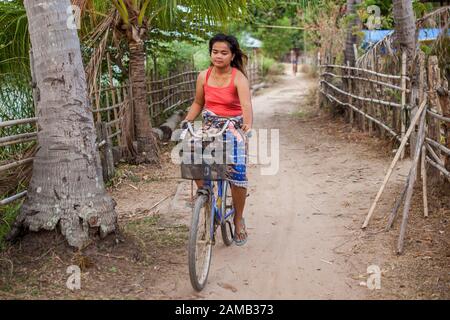 Don DET, LAOS - 5. APRIL 2013: Ein unidentifiziertes Mädchen, das mit dem Fahrrad durch das Dorf Don Dhet, Laos fährt. Stockfoto