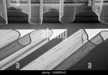 Fensterbank mit vernetzten Vorhängen und Sonne, die durch das Erzeugen von Kurven und Schatten in einer interessanten Darstellung von Licht und Schatten glänzt Stockfoto