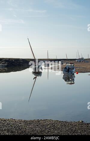 Friedliche Szene von Yachten und Booten in Brancaster Staithes in Norfolk an einem klaren und hellen Tag mit Reflexionen im Stillwasser Stockfoto