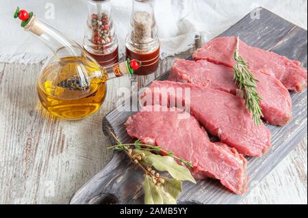 Fleischstücke sind bereit für Marinade liegen auf einer Tontafel mit Gewürzbachtblatt, Pfeffer, provenzalischen Kräutern. Stockfoto