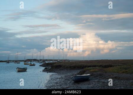 Am frühen Abend im Brancaster Staithes in North Norfolk mit Blick auf das Meer mit Jachten und einem Hintergrund von sonnigen Wolken und hellblauem Himmel Stockfoto