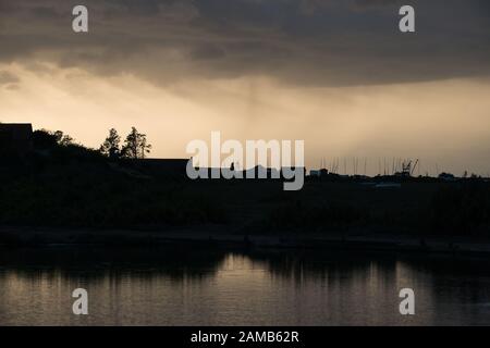 Silhouette von Brancaster Staithes im Norden Norfolks mit Regenwolken, die sich am frühen Abend sonnenlichtend nähern und sich im Wasser niederschlagen Stockfoto