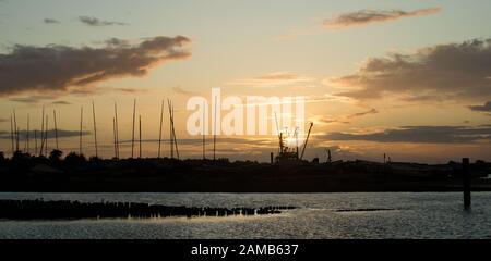Klassisches Bild des Sonnenuntergangs, das eine schöne Silhouette von Brancaster Staithes in North Norfolk erzeugt Stockfoto