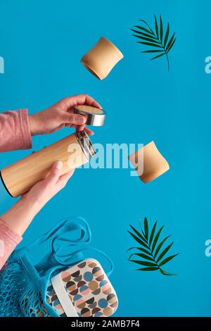 Null Abfall Kaffee in umweltfreundliche isolierte Bambus Kolben. Zwei Hände mit Schale und Palm Leaf, Netztasche mit Mittagessen und Kaffee Kolben fliegen. Null Abfall Stockfoto