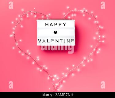 Valentinstag flach lag, Draufsicht auf pinkfarbenem Hintergrund. Leuchtkasten mit Text "Happy Valentine". Helle Girlande in Herzform um die Schachtel herum. Trendy minimalistisch Stockfoto