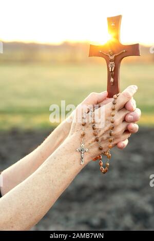 Frau betet bei Sonnenuntergang mit einem Kruzifix im Freien Stockfoto