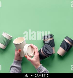 Verschiedene Bambusreisen wiederverwendbare Kaffee- oder Teetassen oder Magen mit Silikonisolierung auf grünem Minzgrund. Hände öffnen den Deckel auf einem Becher. Umweltfreundlich Stockfoto