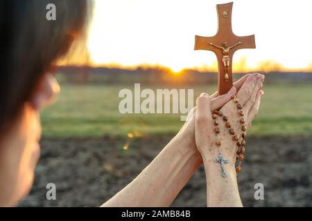 Frau betet bei Sonnenuntergang mit einem Kruzifix im Freien Stockfoto