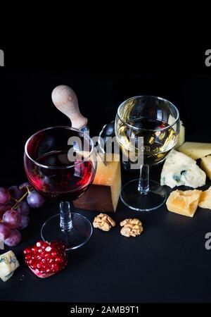 Rot- und Weißwein, Käse, Granatapfel und Trauben auf schwarzem Grund Stockfoto