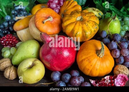 Dekorative Kürbisse, Kürbisse, Äpfel, Birnen, Granatäpfel und Trauben auf dem dunklen Holzhintergrund Stockfoto