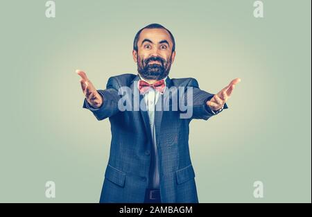 Der stehende, glückliche, bärtige Geschäftsmann fragt, was du getan hast, kommt hierher und umarmt mich, mit der Kamera. Isolierter gleichmäßiger Gradient grün-gelbe Wandrückenergro Stockfoto