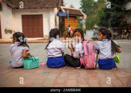 Luang Prabang, Laos - 10. April 2013: Vier Schulmädchen sitzen auf der Bordsteinkante an der Straße in Luang Prabang, Laos. Stockfoto