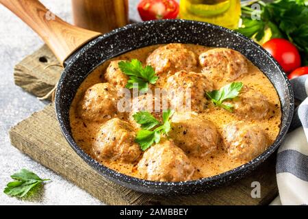Fleischbällchen in Sauerrahm und Tomatensauce in einer Bratpfanne auf Steintisch. Stockfoto