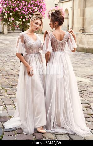 Zwei schöne Brautjungfern Damen in prächtigen eleganten, eleganten, hellgrauen silbernen Bodenlängen offene Hinterkleider in der alten schönen europäischen Stadt auf einem Stockfoto