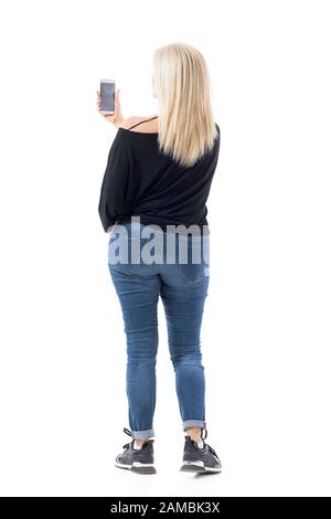 Seitenansicht der legeren Frau im mittleren Alter in Jeans mit Handy oder Fotos. Volle Körperlänge auf weißem Hintergrund isoliert. Stockfoto