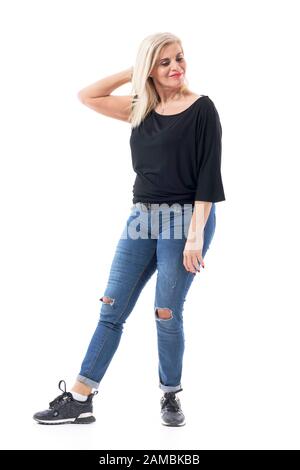 Schöne blonde Mittelaltersfrau in den fünfziger Jahren, die sich entspannend und mit Blick nach unten anrührte. Volle Körperlänge auf weißem Hintergrund isoliert. Stockfoto