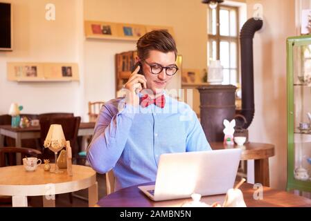 Schuss eines selbstbewussten jungen Mannes, der Hemd und Krawatte trägt, während er im Café am Laptop arbeitet. Kleine Unternehmen. Stockfoto