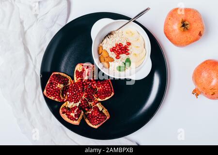 Platte mit gesundem Frühstück von Haferbrei mit Mandeln, Bananen und Granatapfelsamen auf weißem Holztisch, Draufsicht. Stockfoto