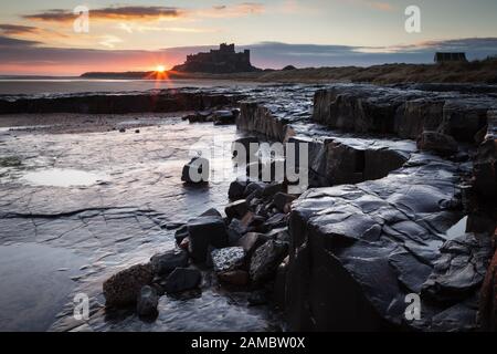 Bamburgh Castle bei Sonnenaufgang mit dunklen nassen Felsen im Vordergrund Stockfoto