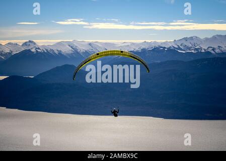 Paragliding über Nahuel Huapi See und Berge von Bariloche in Argentinien, mit verschneiten Gipfeln im Hintergrund. Konzept der Freiheit, Abenteuer, Fliegen Stockfoto