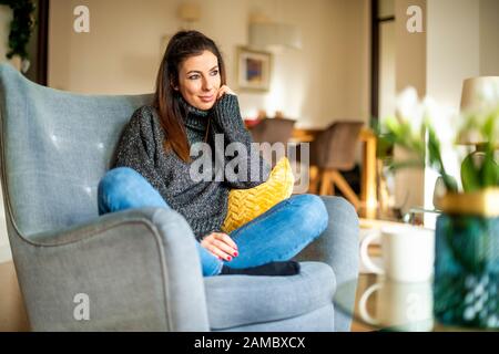Attraktive junge Frau, die daträumt und sich zuhause im Sessel entspannt. Stockfoto