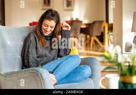 Attraktive junge Frau schüchtern lachen, während sie zu Hause im Sessel entspannen. Stockfoto