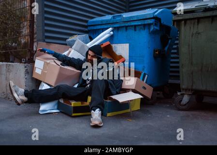 Schmutzig betrunkener Bettler liegt im Müll am Trashcan Stockfoto